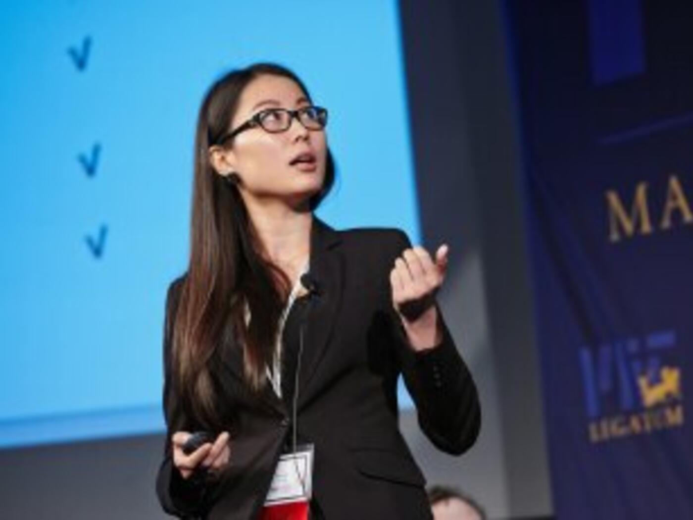 Female presenter standing in front of a blue screen with checkmarks