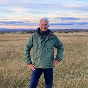 A man poses for a photo in a field beneath the moon during the daytime